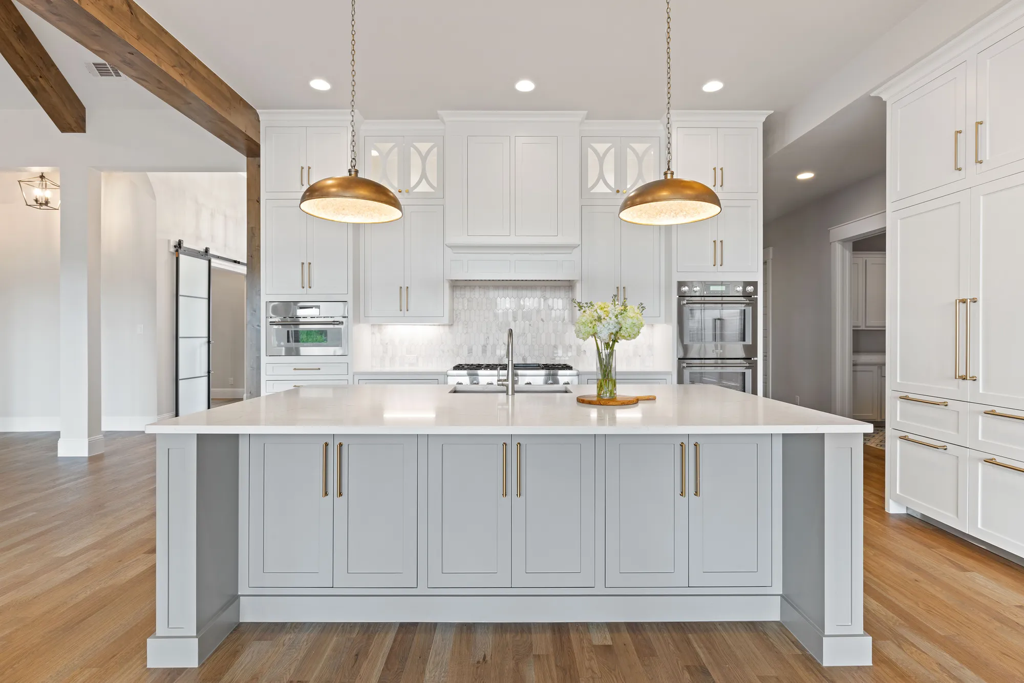 A white shaker kitchen we remodeled, with a large island, brass pendants and a stained wood ceiling beam